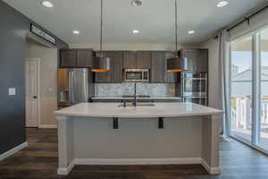 Kitchen with backsplash, recessed lighting, stainless steel appliances, dark brown cabinets, and a kitchen island with sink