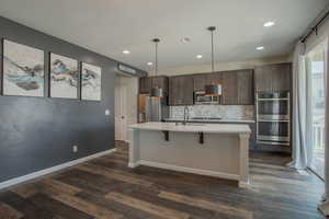 Kitchen with dark brown cabinetry, appliances with stainless steel finishes, decorative backsplash, a kitchen breakfast bar, and decorative light fixtures