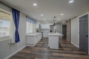 Kitchen with stainless steel appliances, pendant lighting, a barn door, a kitchen island with sink, and white cabinets