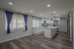 Kitchen featuring a barn door, white cabinetry, a center island with sink, pendant lighting, and appliances with stainless steel finishes