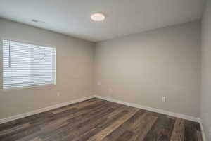 Spare room featuring baseboards and dark wood-style floors