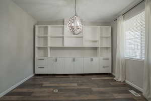 Unfurnished dining area with a chandelier and dark wood-type flooring