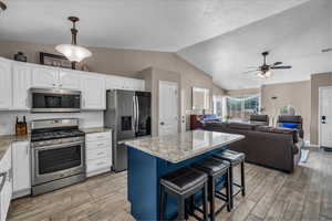 Kitchen with appliances with stainless steel finishes, a kitchen breakfast bar, white cabinets, blue cabinetry, and vaulted ceiling