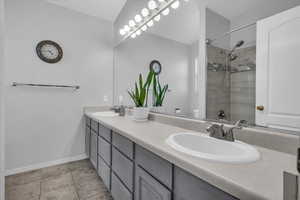 Full bathroom with double vanity, tiled shower, and light tile patterned floors