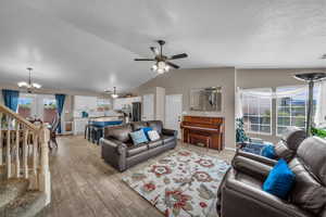 Living area with vaulted ceiling, stairs, light wood-type flooring, a ceiling fan, and a chandelier