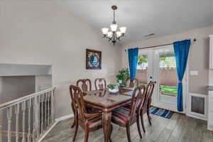 Dining room with light wood finished floors, lofted ceiling, a chandelier, and french doors