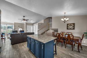 Kitchen with blue cabinets, light stone counters, lofted ceiling, a kitchen island, and decorative light fixtures