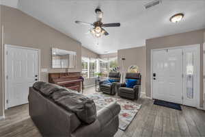 Living room with lofted ceiling, light wood finished floors, a ceiling fan, and a textured ceiling