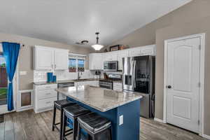 Kitchen with stainless steel appliances, light stone countertops, lofted ceiling, decorative light fixtures, and white cabinets