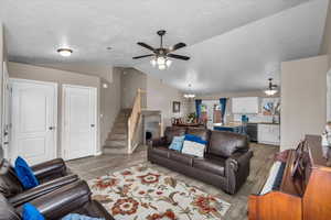 Living area featuring vaulted ceiling, light wood-style floors, a chandelier, a ceiling fan, and stairway