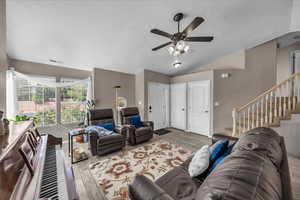 Living area featuring vaulted ceiling, wood finished floors, a textured ceiling, a ceiling fan, and stairway
