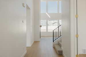 Corridor featuring light wood-style floors, a high ceiling, and stairway