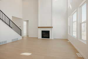 Unfurnished living room featuring a high ceiling, light wood-style floors, a glass covered fireplace, and stairway