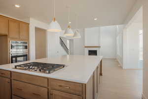 Kitchen featuring pendant lighting, light wood-type flooring, a glass covered fireplace, recessed lighting, and a kitchen island