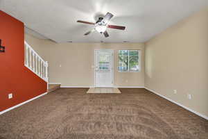 Unfurnished living room featuring carpet, a textured ceiling, stairs, and ceiling fan