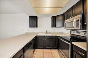 Kitchen featuring stainless steel appliances, light countertops, light tile patterned flooring, a textured ceiling, and dark cabinetry