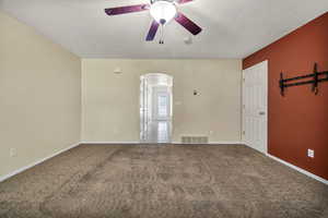 Carpeted spare room with ceiling fan, arched walkways, and a textured ceiling
