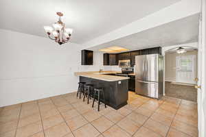 Kitchen featuring appliances with stainless steel finishes, light tile patterned flooring, light countertops, a breakfast bar, and a peninsula