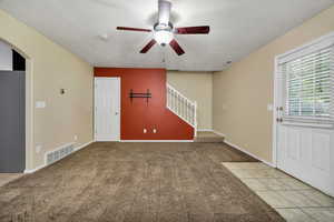 Unfurnished living room featuring light tile patterned floors, light colored carpet, ceiling fan, stairway, and a textured ceiling