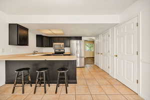 Kitchen featuring arched walkways, light countertops, a kitchen breakfast bar, stainless steel appliances, and light tile patterned floors