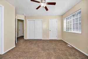 Unfurnished bedroom with dark carpet, a closet, and a ceiling fan
