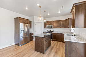 Kitchen featuring dark brown cabinetry, dark stone countertops, appliances with stainless steel finishes, pendant lighting, and recessed lighting