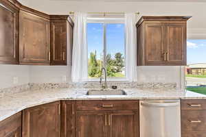 Kitchen featuring dishwasher, plenty of natural light, light stone counters, and dark brown cabinetry