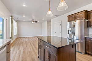 Kitchen with dark stone counters, stainless steel fridge, pendant lighting, light wood-style flooring, and recessed lighting