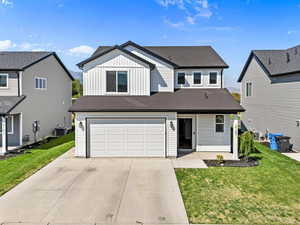 View of front of house featuring board and batten siding, concrete driveway, roof with shingles, and a front yard