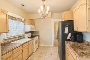 Kitchen with light brown cabinets, white appliances, decorative light fixtures, light tile patterned flooring, and a chandelier