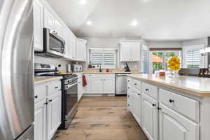 Kitchen featuring appliances with stainless steel finishes, white cabinetry, recessed lighting, light wood-type flooring, and a center island