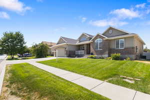View of front of property with brick siding, covered porch, driveway, a front yard, and a garage
