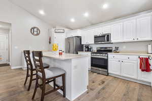 Kitchen featuring vaulted ceiling, stainless steel appliances, a breakfast bar, recessed lighting, and white cabinets