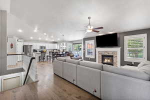 Living room with dark wood-type flooring, vaulted ceiling, a stone fireplace, and a ceiling fan