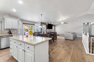 Kitchen with white cabinetry, light wood finished floors, stainless steel dishwasher, vaulted ceiling, and a kitchen island