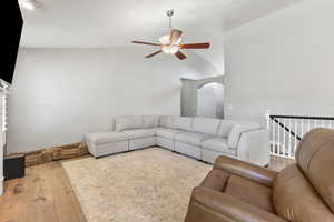 Living area with hardwood / wood-style flooring, ceiling fan, arched walkways, and high vaulted ceiling