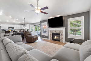Living room with vaulted ceiling, wood finished floors, a fireplace, and ceiling fan