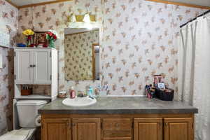 Bathroom featuring wallpapered walls, a textured ceiling, vanity, and ornamental molding