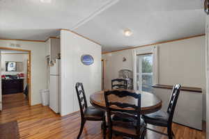 Dining area with light wood finished floors, crown molding, and a textured ceiling