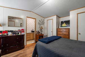 Bedroom featuring vaulted ceiling, light wood-type flooring, ornamental molding, and a textured ceiling