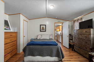 Bedroom with ornamental molding, lofted ceiling, wood finished floors, and a textured ceiling