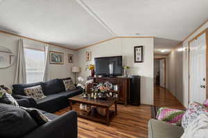 Living room with wood finished floors, vaulted ceiling, ornamental molding, and a textured ceiling