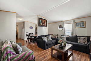 Living area featuring lofted ceiling, wood finished floors, a textured ceiling, and crown molding