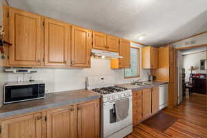 Kitchen with white appliances, dark wood-style flooring, a textured ceiling, lofted ceiling, and under cabinet range hood