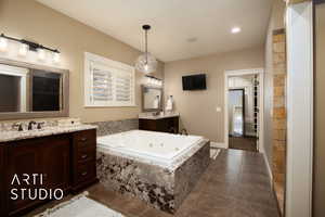 Bathroom featuring vanity, a tub with jets, dark tile patterned floors, and recessed lighting