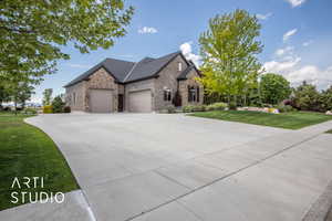 View of front of home featuring a front yard, stone siding, an attached garage, and driveway