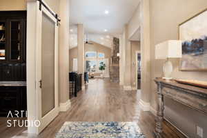 Hallway with a barn door, light wood finished floors, recessed lighting, and high vaulted ceiling