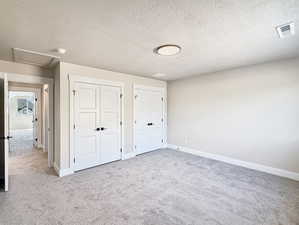 Unfurnished bedroom with multiple closets, a textured ceiling, attic access, and light colored carpet