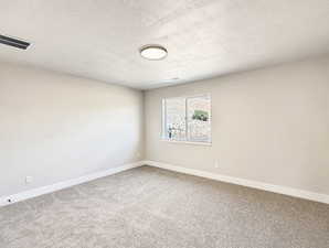 Empty room with light colored carpet and a textured ceiling