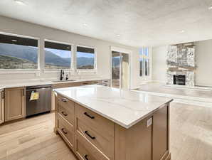 Kitchen featuring light wood-style flooring, a textured ceiling, a mountain view, dishwasher, and light stone counters